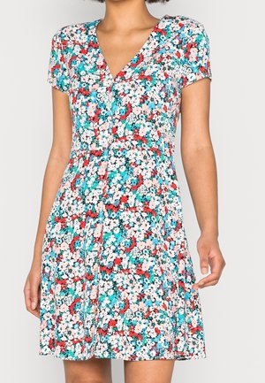 Woman wearing a short-sleeve, V-neck dress with a multicolor floral pattern in red, white, pink, blue, and green on a light background.
