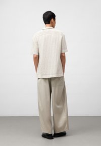 Kortaf shirts in lichtbeige met verticale strepen, gecombineerd met losse, lichtgrijze broeken. De stof lijkt gestructureerd en ademend.