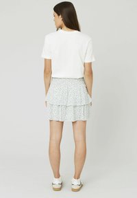 Un t-shirt blanc à manches courtes associé à une jupe à volants à imprimé floral bleu. La jupe a une taille froncée et un ourlet à volants. Des baskets blanches.