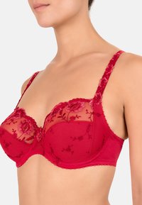 Rode beha met doorzichtige mesh cups, voorzien van bloem- borduursel, kantafwerking en verstelbare bandjes. Gladde band biedt ondersteuning en comfort.