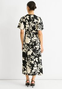 Schwarz-weißer Blumendruck-Maxi-Kleid mit kurzen, rüschierten Ärmeln, tailliertem Schnitt und einem Bindegürtel. Glatte Textur, knöchellanges Design.
