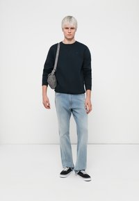 Hanorac bleumarin, blugi deschiși, adidași negri și o geantă crossbody gri cu un finisaj texturat și accente metalice.