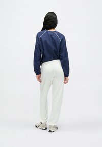 Μπλε σκούρο, ελαφρύ μπλουζάκι με μακριά μανίκια και ασημί λεπτομέρειες· ανοιχτό γκρι, άνετη φόρμα· sneakers σε ουδέτερους τόνους.