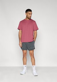 Ανδρικό μακρυμάνικο μπλουζάκι Nike σε βυσσινί απόχρωση, συνδυασμένο με σκουρόχρωμο γκρι, υφασμάτινο σορτς με λογότυπο, λευκές κάλτσες και λευκά αθλητικά παπούτσια.