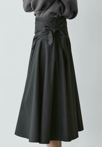 Zwarte midi-rok van zachte stof, voorzien van een ceintuur met strik en een uitlopende pasvorm. Aan de achterkant zit een ritssluiting voor sluiting en een flatterend silhouet.