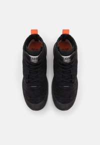 Baskets montantes en tricot noir avec col élastique, présentant une surface texturée, un onglet de talon orange et une semelle en caoutchouc noire.