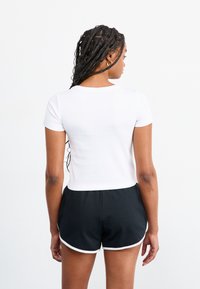 Hvit kortermet topp kombinert med svarte treningsshorts med hvite detaljer. Toppen har en tettsittende design og rund hals.