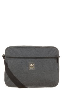 Šedá textilní messenger taška s přední kapsou na zip, nastavitelným černým ramenním popruhem a zlatou panelou s logem Adidas. Obdélníkový design.