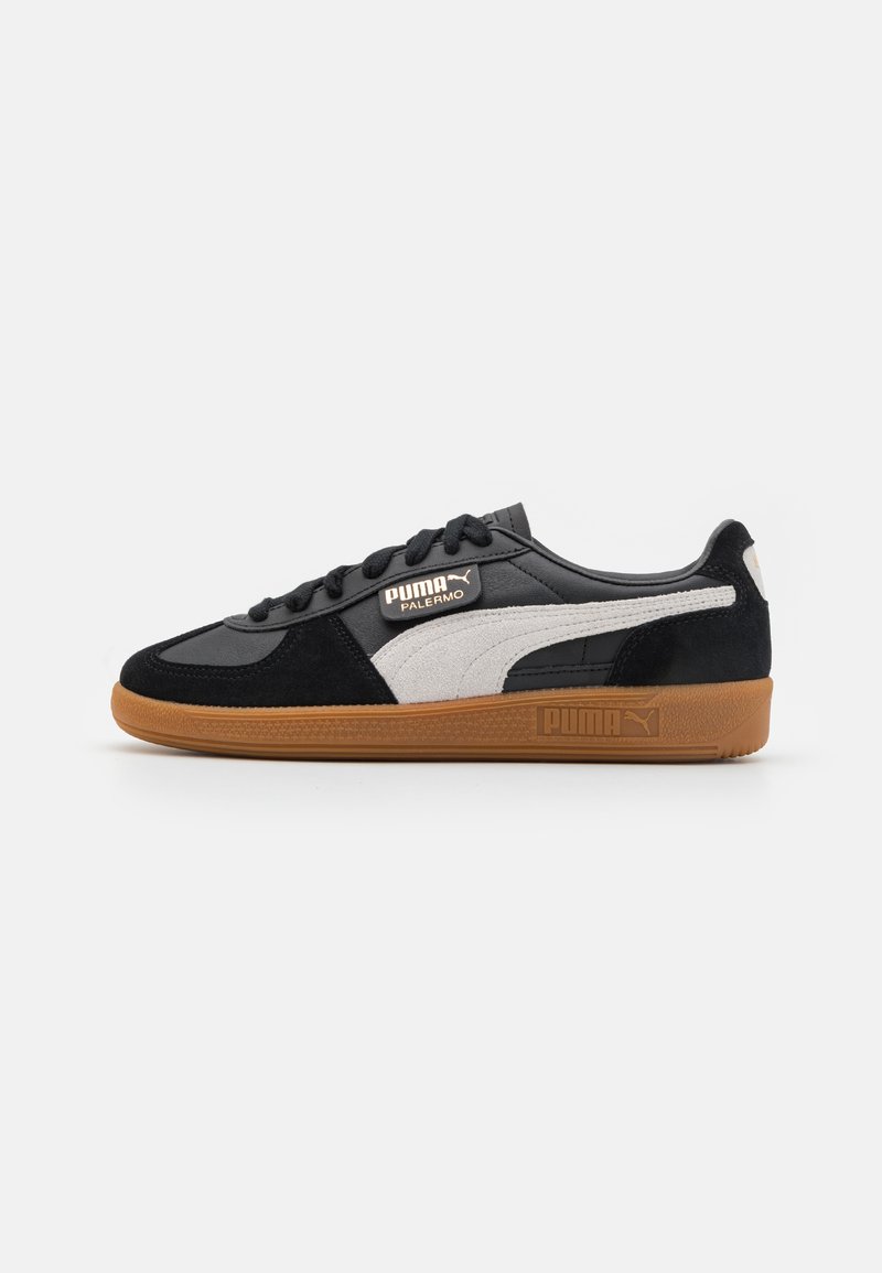 Sneaker nero e grigio con tomaia in suede e pelle, dettaglio a striscia bianca e suola in gomma marrone. Presenta un logo PUMA sul lato.
