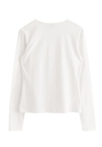 Vit långärmad T-shirt med rund halsringning och en mjuk, len yta. Designen är enkel utan ytterligare mönster eller detaljer.