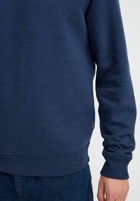 Felpa blu navy con una texture morbida, polsini e orlo a costine, con un piccolo logo del marchio sul lato. Vestibilità standard e design a girocollo.