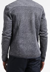 Giacca in fleece grigia e testurizzata con design aderente e maniche lunghe. Presenta un leggero motivo a spina di pesce e cuciture piatte.