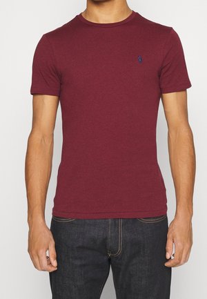 Bordowa koszulka z krótkim rękawem, wykonana z miękkiej tkaniny, z okrągłym dekoltem i małym niebieskim logo na lewej piersi. Luźny fason.