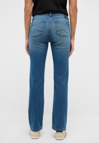 Zili džinsu bikses ar taisnu kāju griezumu, kurās ir divas aizmugurējās kabatas un izbalējuma detaļas gar kājām.