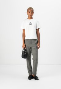 White short-sleeve t-shirt with a black smiley face print, gray tapered trousers, black mini handbag, and black slip-on shoes.