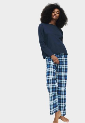 Maglietta a maniche lunghe blu navy abbinata a pantaloni da pigiama a quadri nei colori blu, nero e bianco. Tessuto morbido con vestibilità ampia, senza hardware visibile.