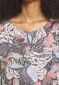 Floral-patterned fabric in soft pink, featuring intricate leaves in green, blue, and brown. Round neckline, lightweight material.