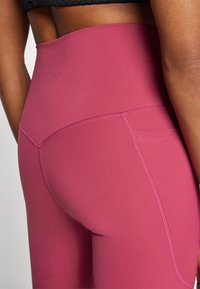 Leggings taille haute d'une couleur magenta unie, avec un tissu extensible, des coutures plates et un détail de poche arrière discret.