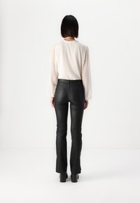 Pantaloni negri din piele ecologică, cu talie înaltă și picioare evazate, asortați cu o bluză ușoară cu mâneci lungi, care are o textură subtilă și un decolteu cu volănașe.