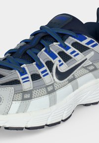 Μπλε, γκρι και λευκό αθλητικό παπούτσι Nike για τρέξιμο με πλεκτό επάνω μέρος, πολλαπλές θηλιές για κορδόνια και μαύρο λογότυπο Swoosh στο πλάι.