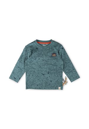 Grünes Langarmshirt mit geometrischen schwarzen Mustern, Rundhalsausschnitt und kleinem braunen Logo auf der Brust. Enthält ein Stoffetikett und ein tierisches Accessoire.