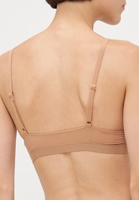 Nude bh med justerbare stropper, et glatt, elastisk stoff og et enkelt design med sømløs bak for komfort og støtte.