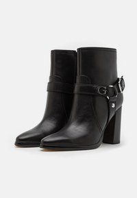 Czarne skórzane botki za kostkę z ostrogą, grubym obcasem oraz ozdobnym paskiem z srebrną klamrą i logo. Gładka faktura.
