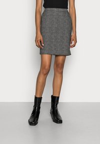 Mini gonna a quadri grigia con un design aderente. Indossata con stivali alla caviglia neri. Tessuto morbido e dettagli del pattern sottili.