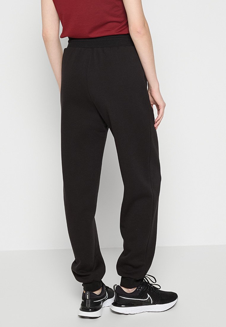 Pantalons de jogging noirs avec un design effilé, une taille élastique, des poches latérales et des poignets côtelés, associés à des baskets noires.