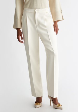 Pantaloni bianchi a vita alta con pieghe, realizzati in un tessuto morbido. Abbinati a tacchi a stiletto color crema con dettagli dorati.