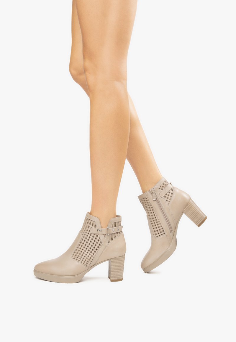 Stivaletti beige alla caviglia con una tomaia texturizzata, lati perforati, chiusura con zip, tacco spesso e un dettaglio con cinturino regolabile.