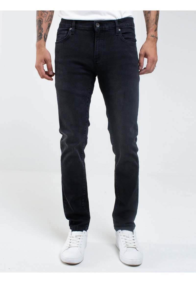 Čierne riflové nohavice so slim fit strihom, päť vreciek, minimálnym šitím a zapínaním na gombík. Skombinované s bielymi teniskami.