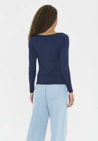 Top de manga larga azul marino con escote redondeado, de corte ajustado. Combinado con unos vaqueros de pierna ancha de color azul claro. La tela parece suave y con detalles mínimos.