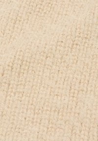 Primo piano di tessuto lavorato a maglia morbido color crema con una texture pelosa e un motivo a coste verticali.