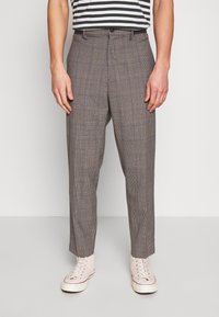 Hnědé kostkované kalhoty s volným střihem, s plochým předním dílem, poutky na opasek a jednobodovým zapínáním, doplněné bílými teniskami.