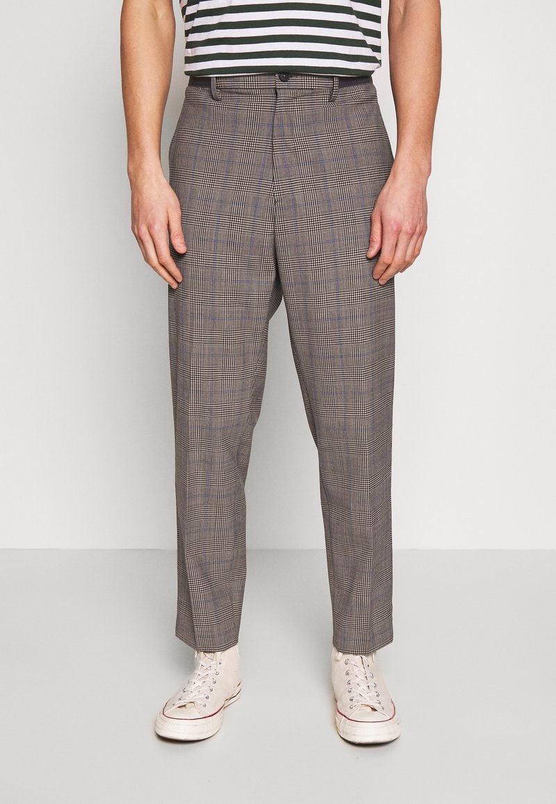 Hnědé kostkované kalhoty s volným střihem, s plochým předním dílem, poutky na opasek a jednobodovým zapínáním, doplněné bílými teniskami.