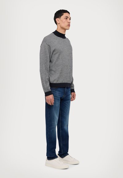Maglione grigio e bianco con motivo, dotato di un colletto scuro, abbinato a jeans in denim blu e sneakers bianche, mostrato in vista laterale.