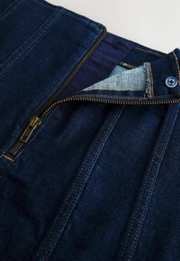 Dark blue denim skirt featuring a gold zipper and blue fabric lining exposed at the waist. Noticeable orange stitching along seams.