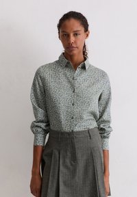 Zielona koszula w kwiatowy wzór z kołnierzykiem zapinanym na guziki, długimi rękawami i luźnym krojem, zestawiona z szarą spódnicą w cienkie prążki.