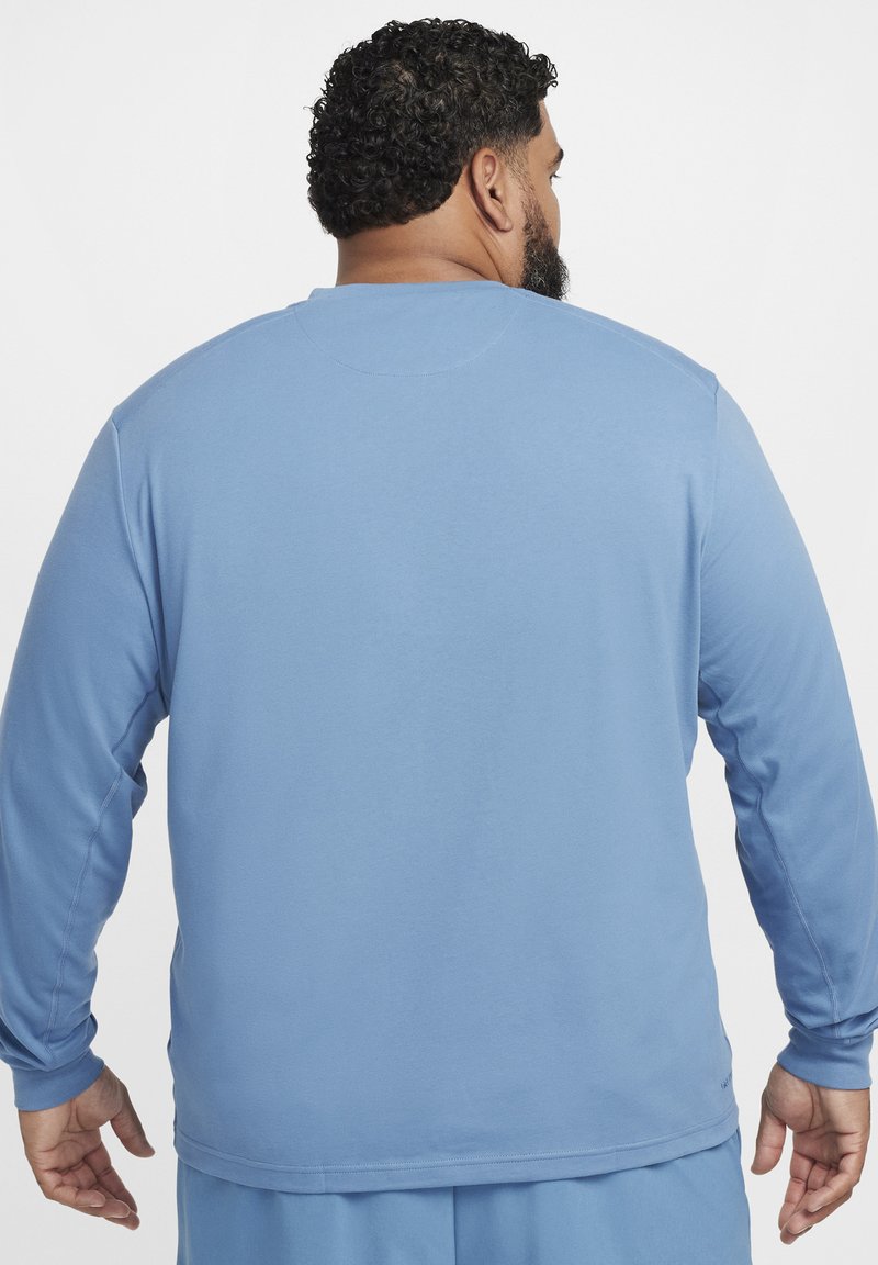 Jasnoniebieska bluzka z długim rękawem, uszyta z miękkiej tkaniny, z okrągłym dekoltem i przeszytymi detalami. Tył jest gładki, a fason luźny.