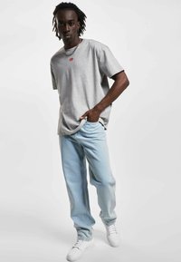 Grå bomull t-skjorte med korte ermer og rødt logo, kombinert med lys blå denimbukser og hvite sneakers, med en avslappet passform.