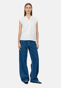 Fehér, rövid ujjú felső V-nyakkal és puha textúrával. Kék, bőszárú farmernadrág klasszikus denim varrással. Fekete, hegyes orrú cipő.