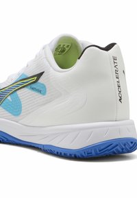 Zbliżenie na biały but do biegania z niebieską podeszwą, czarno-żółtym logo, zielonym wnętrzem i napisem "ACCELERATE" na pięcie.