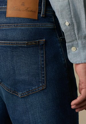 Donkerblauwe denimjeans met een gladde textuur. Kenmerken zijn onder andere een leren label op de tailleband en een achterzak met stikdetails.