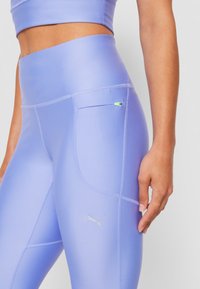 Detailní záběr osoby v světle fialových vysokých legínách s boční kapsou a logem Puma, zobrazuje část ladícího kratšího topu.