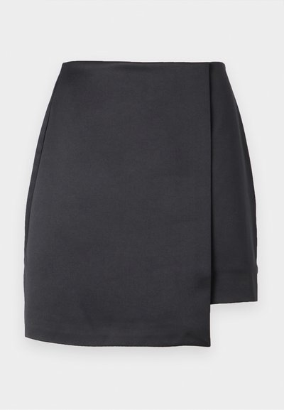 Mini-jupe asymétrique noire avec un pan avant style portefeuille sur fond blanc.