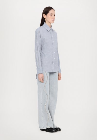 Lys blå skjorte med krage, kombinert med lyse denimjeans som har en bølgete rhinestones accent langs sidesømmene.
