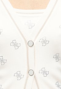Cardigan blanc côtelé avec de gros boutons argentés et un motif répétitif de petits dessins floraux en strass.