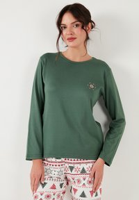 Top verde cu mânecă lungă, cu decolteu rotund și un mic detaliu de broderie florală pe partea stângă. Material neted, croi lejer și stil casual.