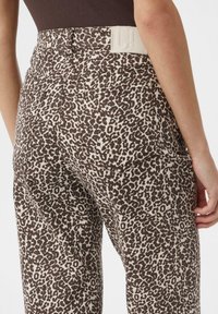Spodnie w brązowo-kremowy wzór panterki z wysokim stanem, z tylkimi kieszeniami i fakturowanym pasem. Wykonane z miękkiego materiału o luźnym kroju.